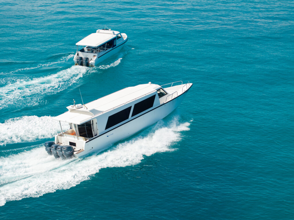 Aerial view of two high-speed white transfer boats accelerating across the clear turquoise water, demonstrating the fast and reliable Maldives private speedboat charter fleet.